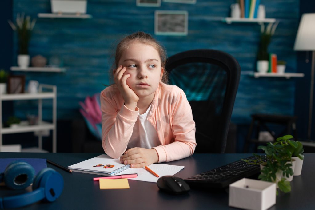 A young girl is inattentive and daydreaming over a notepad.