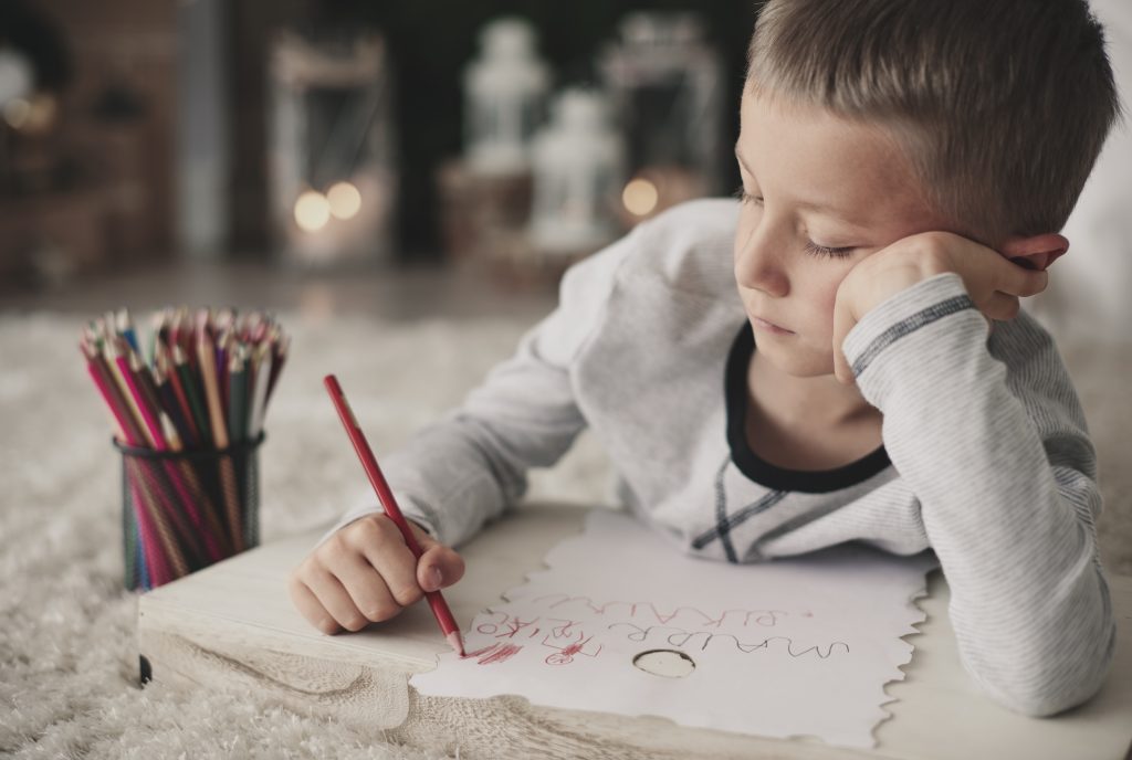 Young boy looks bored while drawing.