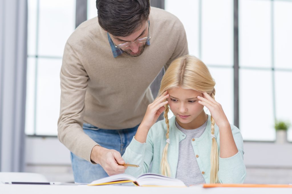 A young girl struggles with frustration intolerance while her dad looks over her shoulder and offers support.