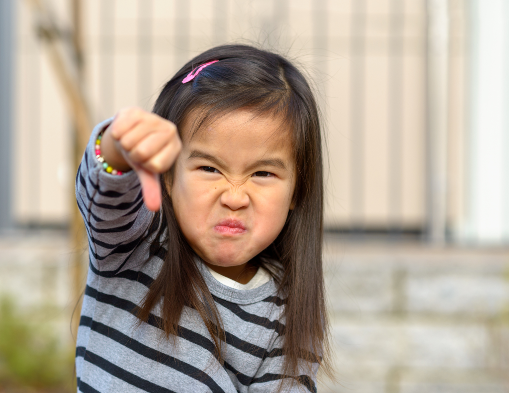 PDA in ADHD and autistic kids manifests with little girl giving the thumbs down and a grumpy face