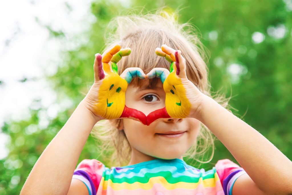 Child with paint on hands makes a heart