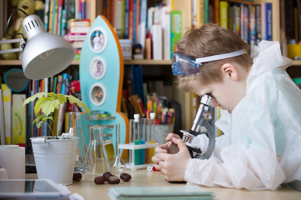 Boy looks into a microscope as he studies science at home
