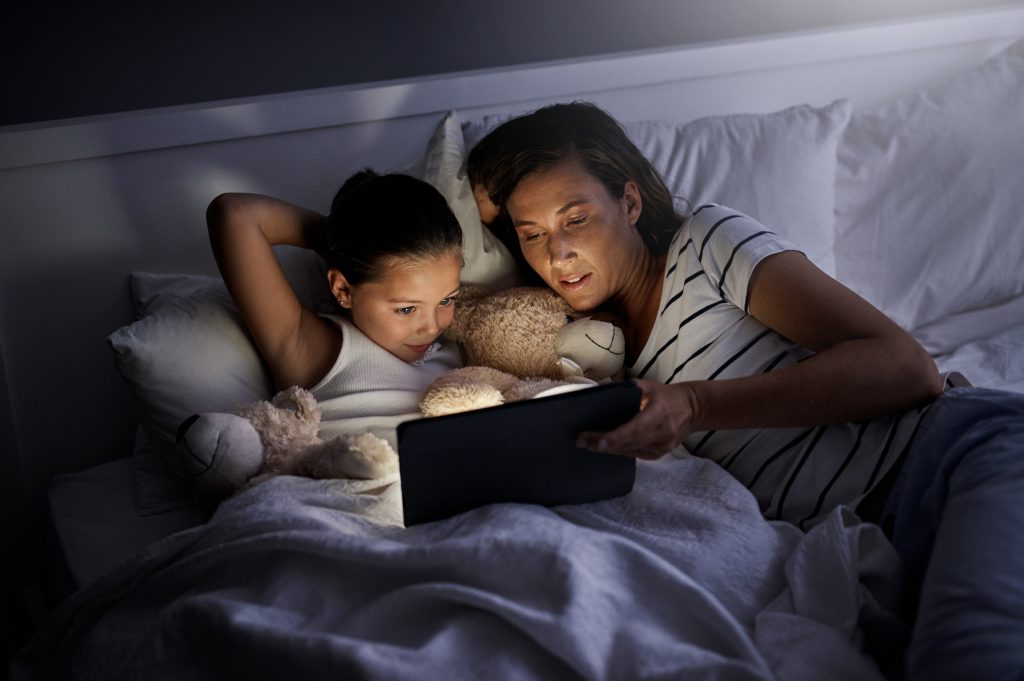 Mother and daughter snuggling and reading in bed at night